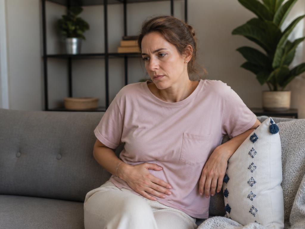 Frau um die 40 sitzt nachdenklich und erschöpft auf dem Sofa